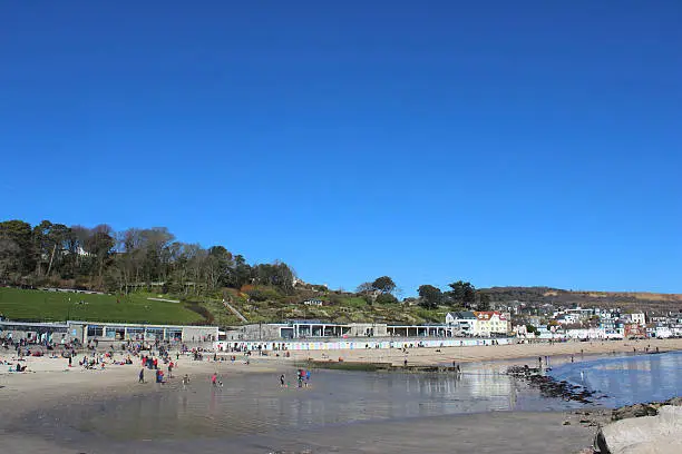 Photo showing the sunny beach town of Lyme Regis, which is located within the county of Dorset, England, UK, where it is known for its sandy beachfront and fossil hunting heritage.