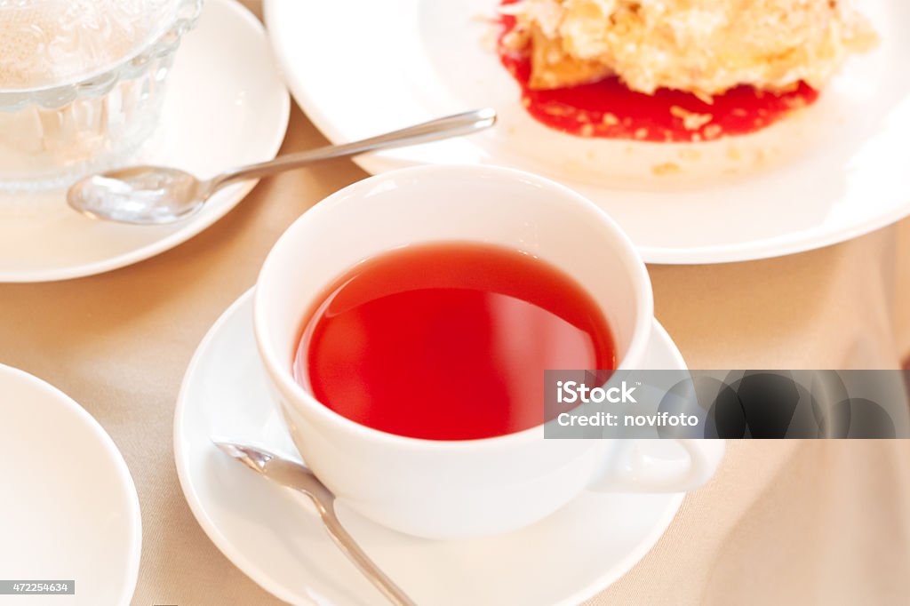 Cup of tea. Elegant white cup of tea on a table in a restaurant. Table covered with beige cloth. On the table dishes: plates with dessert, metal devices, 2015 Stock Photo