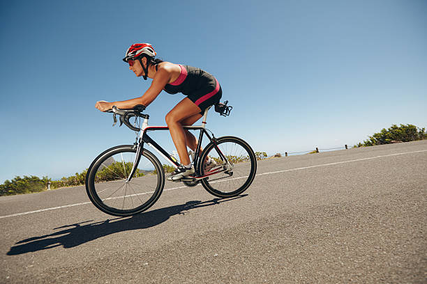 Female cyclist on a country road training for competition. Young woman riding bicycle down hill.