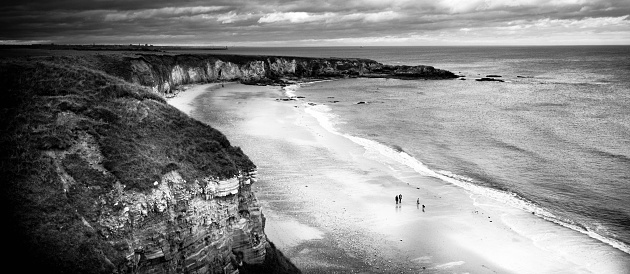 Black and white panoramic seascape with waves flowing between rocks.