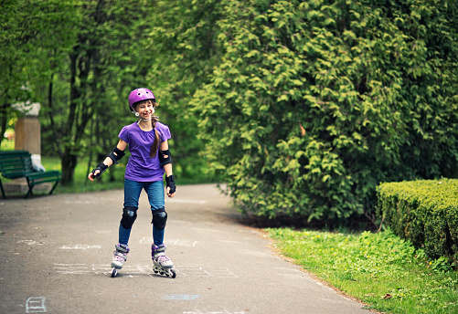 Happy little girl learning to rollerblade in a sunny park. The girl aged 9 is laughing while riding the rollerblades.