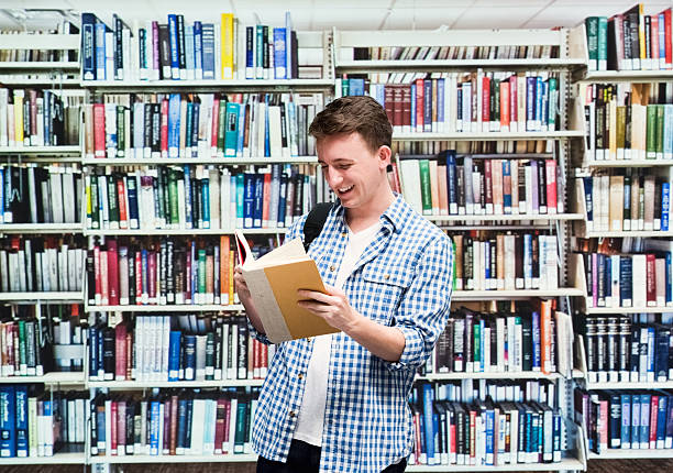 istock Smiling male student reading book in library 472293752
