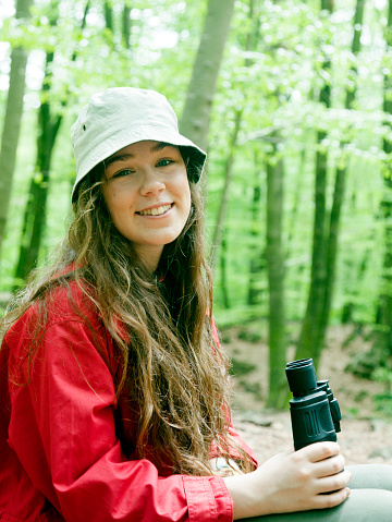 Young girl in a beech forest, smiling and holding binoculars.