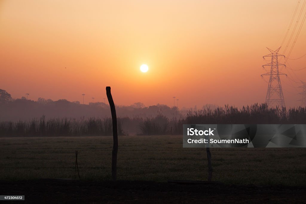 Sunset over agricultural land and a huge transmission line Sunset over agricultural land making the sky look red in colour. The foreground is dark. Bushes and trees are visible in the horizon. A huge high voltage transmission line is seen on the side. 2015 Stock Photo