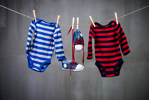 Two striped baby onesies and baby shoes hanging on the clothesline