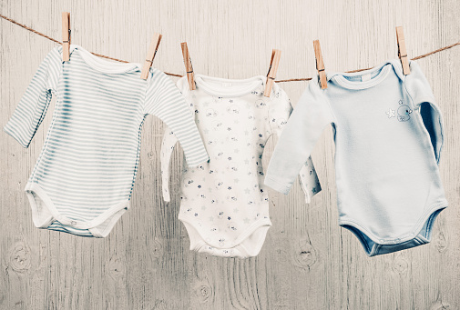 Three cotton baby onesies hanging on the clothesline and white vintage wooden background