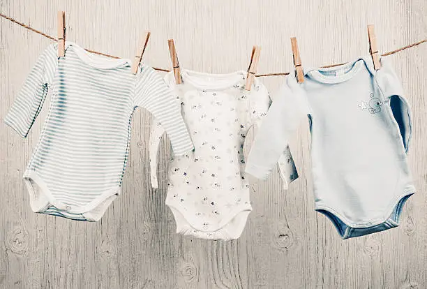 Three cotton baby onesies hanging on the clothesline and white vintage wooden background
