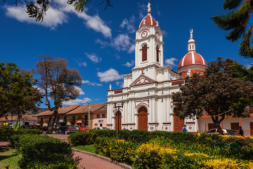 Subachoque, Colombia - January 02, 2015: The  Roman Catholic church on the main square, in the Andean town of Subachoque, in the South American country of Colombia. It is typical of Spanish Colonial architecture in Latin America. A few local people can be seen going about their daily chores.  There are some shops, a bank and restaurants by the side of the church. Photo shot from the park on the main town square, in the early afternoon sunlight against a bright blue andean sky; horizontal format.