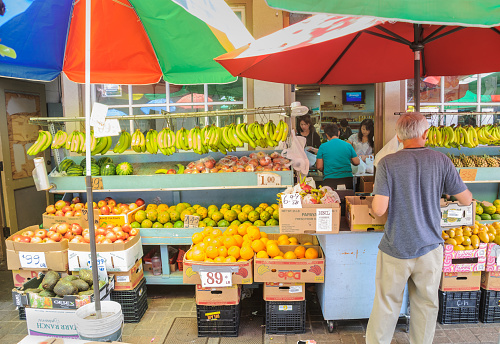 Honolulu, Hawaii. USA- April 20, 2015: A man in a grey t-shirt  makes a selection of fresh  fruit at a sidewalk display  as other customers get their purchases weighed inside in the Chinatown neighborhood of Honolulu, Hawaii