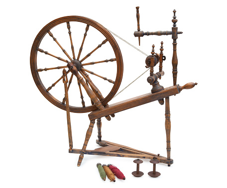 An antique wooden spinning wheel with yarn and bobbins isolated on a white background