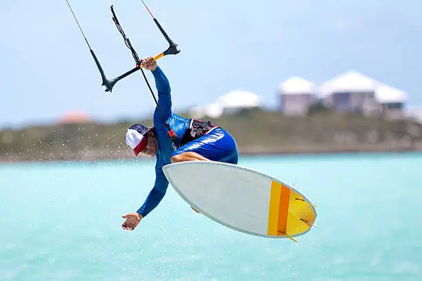 A kitesurfer performing an aerial trick riding strapless surfboard on a sunny day.