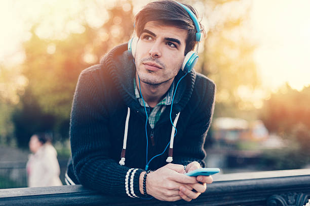 An African American man is putting her wireless headphones on while walking in the city