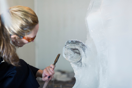 Women working with work tool, cutting ice block, making ice sculpture. Selective focus to ice sculpture.