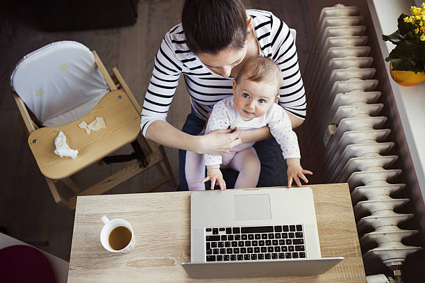 Overhead view of young mother working on computer with baby