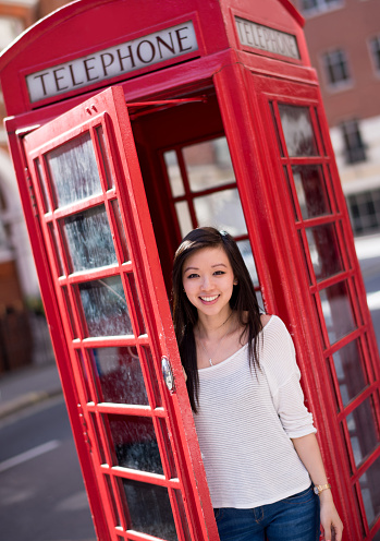 Young Asian woman in London inside a telephone booth and looking at the camera