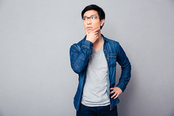 istock Pensive asian man standing over gray background 472348398