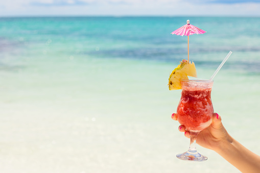 Woman holding alcoholic cocktail on tropical beach.