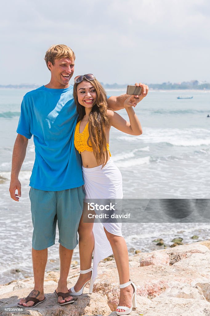 Young Happy Couple Taking Selfie Self Portraits at the Beach Happy young couple taking selfie self portrait photos on vacation at a tropical beach in Kuta, Bali, Indonesia, 20-29 Years Stock Photo