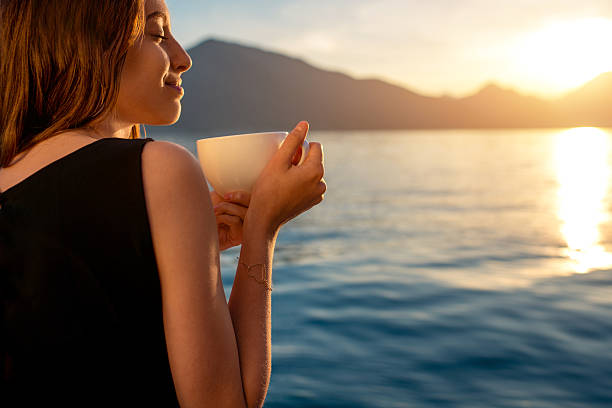 istock Young woman drinking coffee on the pier at sunrise 472354672