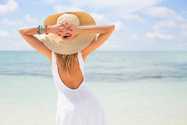 młoda kobieta w białą sukienkę na plaży - kapelusz słoneczny zdjęcia i obrazy z banku zdjęć