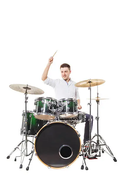 Handsome guy behind the drum kit on a white background in shirt and trousers