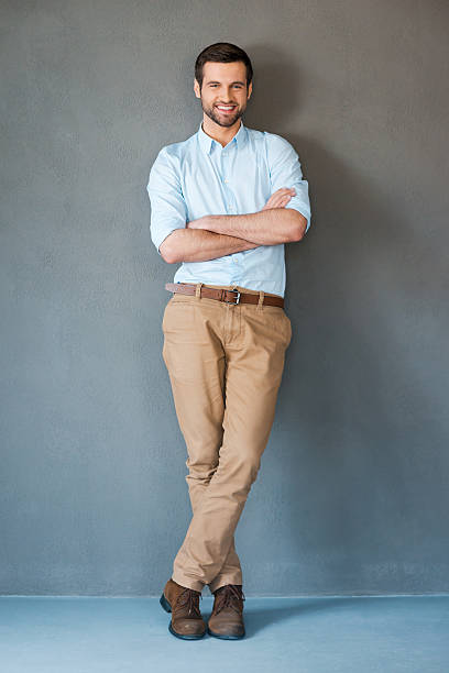 Smiling man with arms crossed facing the camera Full length of handsome young man in shirt keeping arms crossed and smiling at camera while standing against grey background business casual fashion stock pictures, royalty-free photos & images