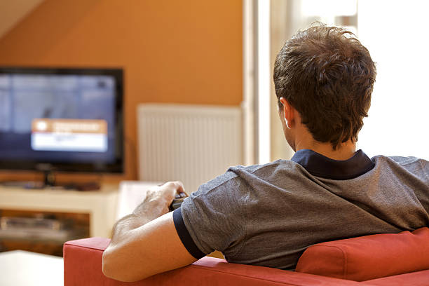 istock Rear view of young man watching television 472363372