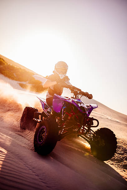 istock Quad racer maneuvering over sand tracks with sun flare behind 472366996