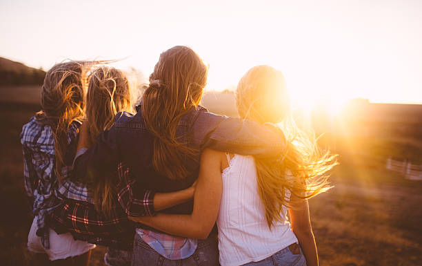 Teen girls facing the sunset with on a summer evening Rearview of teen girl friends looking at the sunset together on a golden summer evening arm in arm stock pictures, royalty-free photos & images