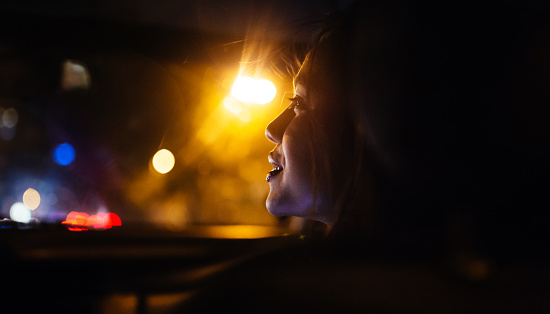 Smiling Asian girl sitting in the passenger seat of a car driving around the city at night