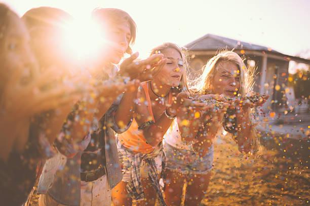 istock Teens blowing colourful confetti together outdoors with sun flare 472367036