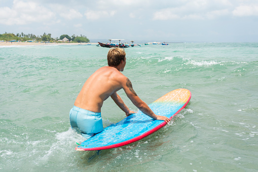 Young man about to paddle a surf board in Bali, Indonesia.