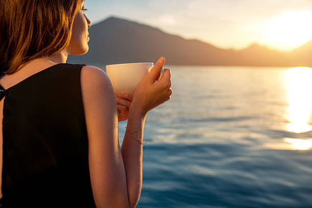 istock Young woman drinking coffee on the pier at sunrise 472376630