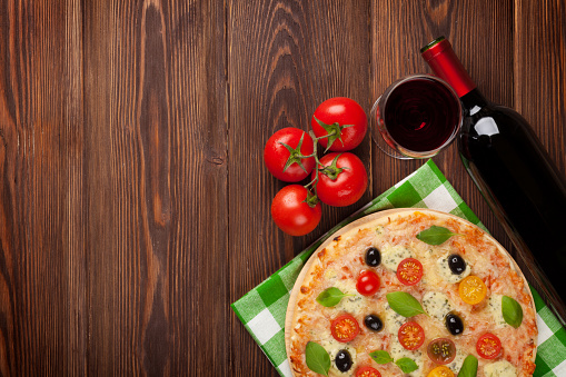 Pizza and red wine on wooden table background. Top view with copy space
