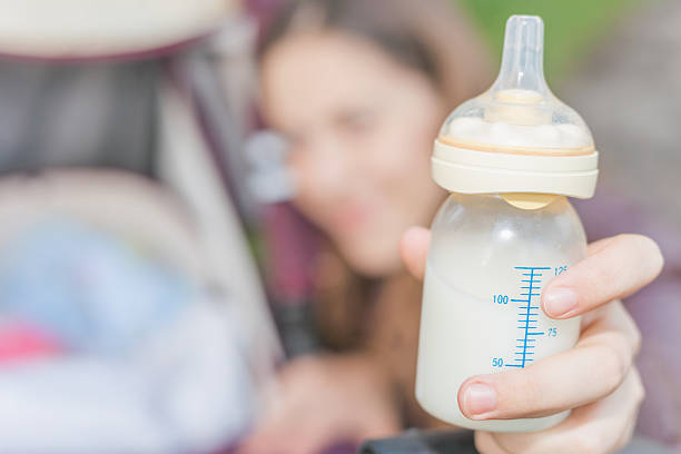 background of happy mom holding at hand baby bottle with milk at foreground