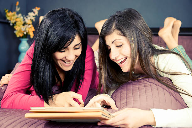 istock Happy girlfriends playing with tablet in bed 472388178