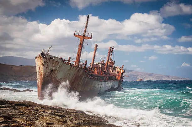 Abandoned, covered in rust shipwreck being hit with huge waves during a sea storm on Andros island in Greece