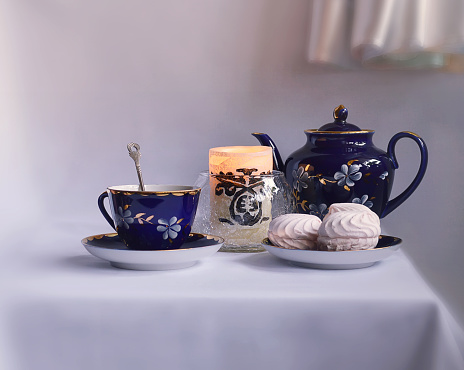 Tea Party of cobalt glassware Cup of tea, three marshmallow on a saucer, teapot and burning candle on the table.