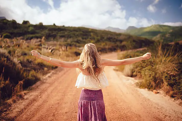 Rearview shot of a boho girl standing with her arms outstretched freely on a country dirt road