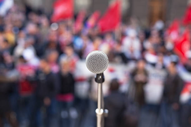 istock Microphone in focus against unrecognizable crowd of people 472397438