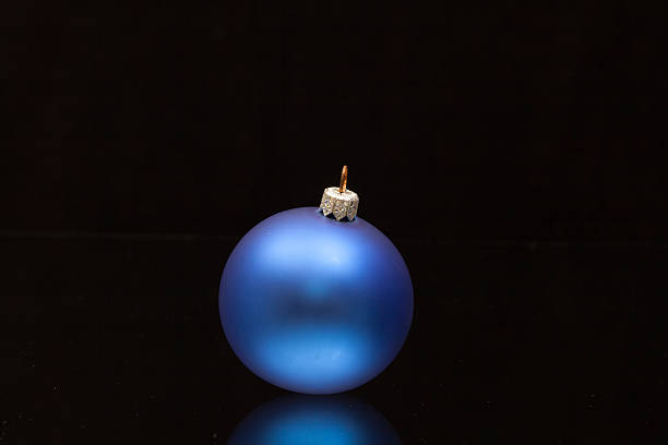 Closeup of frosted royal blue Christmas ball with winter theme cap. Christmas ornament illuminated from top. Christmas decoration, festive atmosphere concept.
