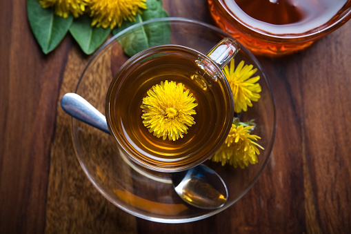 dandelion tisane tea with fresh yellow blossom inside tea cup, on wooden table