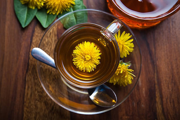 dandelion tisane tea with yellow blossom inside teacup dandelion tisane tea with fresh yellow blossom inside tea cup, on wooden table dandelion root stock pictures, royalty-free photos & images