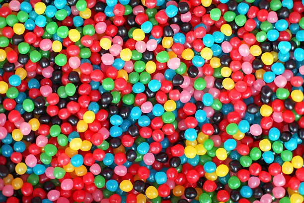 This is a full frame top view image of jelly bean candy in variety of colors, including red, pink, green, yellow, blue, and black. Colorful jellybean wallpaper pattern or a background.