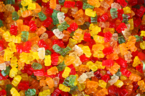 This is a full frame top view image of gummy bears in variety of colors, including red, green, yellow, orange, and white. Gummy Bear background.