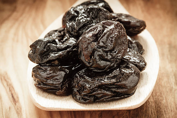 istock dried plums prunes on wooden spoon 472475710