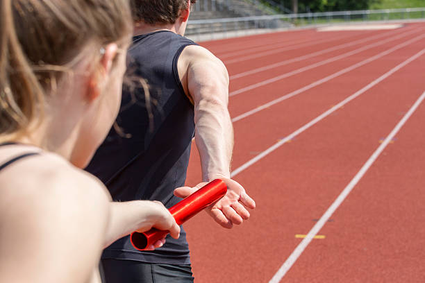 A relay race handing over the baton to a male runner Relay race handing over from woman to man. Unfiltered version relay photos stock pictures, royalty-free photos & images
