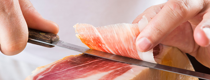 Professional cutter carving  slices from a whole bone-in serrano ham