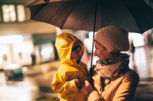 Photo of mother and son in one rainy evening. They are standing under umbrella.