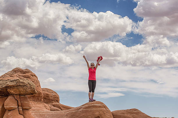 Teenage girl on desert rocks, arms in air stock photo